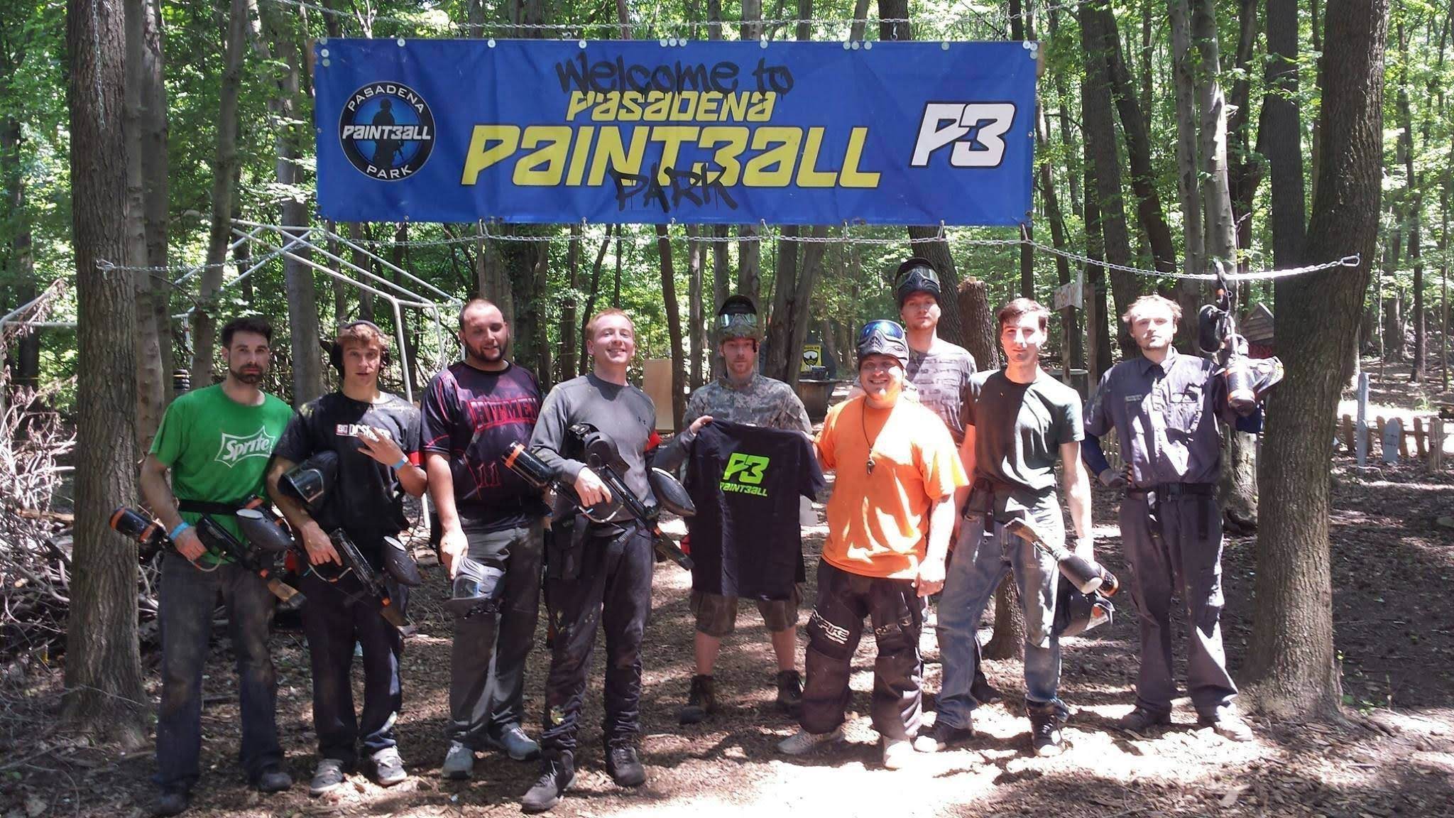 Nine men stand together in a forest setting for a group photo under a banner that reads 